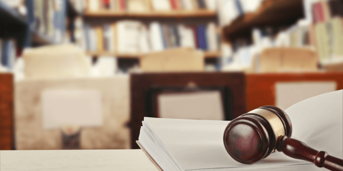 Hölzerner Richterhammer, der auf dem Gesetzbuch auf dem Tisch in der Bibliothek liegt